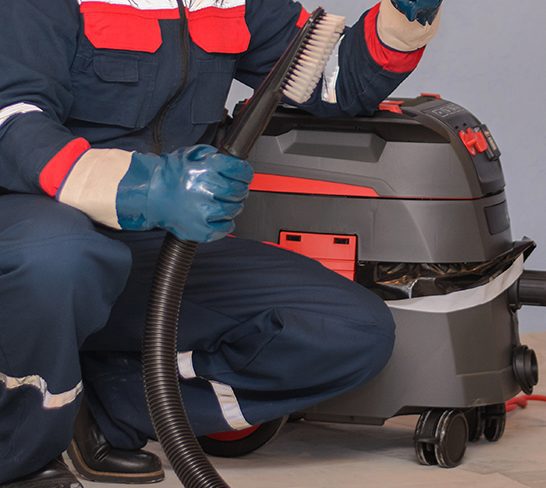 Man Vacuuming a Construction Site. Closeup of a cleaner in special clothes and rubber gloves holds a brush from an industrial professionally vacuum